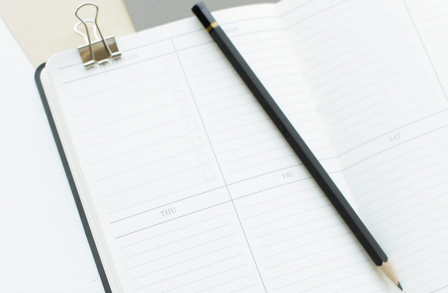 From above opened notebook with empty sheets and black pencil placed on white desk